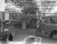 Interior view of unidentified car assembly plant, showing assembly line works, chassis, and workers